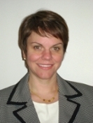 A profile of a smiling woman with short brown hair wearing a gray blazer and white blouse.