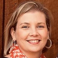 A profile of a smiling woman with blonde hair wearing hoop earrings and a patterned scarf.